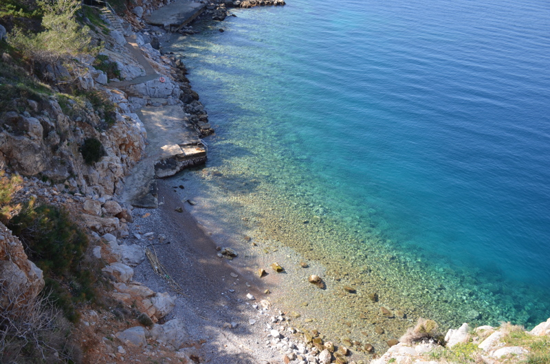 Avlaki Beach, a quiet, pebbled cove nestled along the rocky coastline of Hydra, Greece, famous for its exceptionally clear, turquoise waters